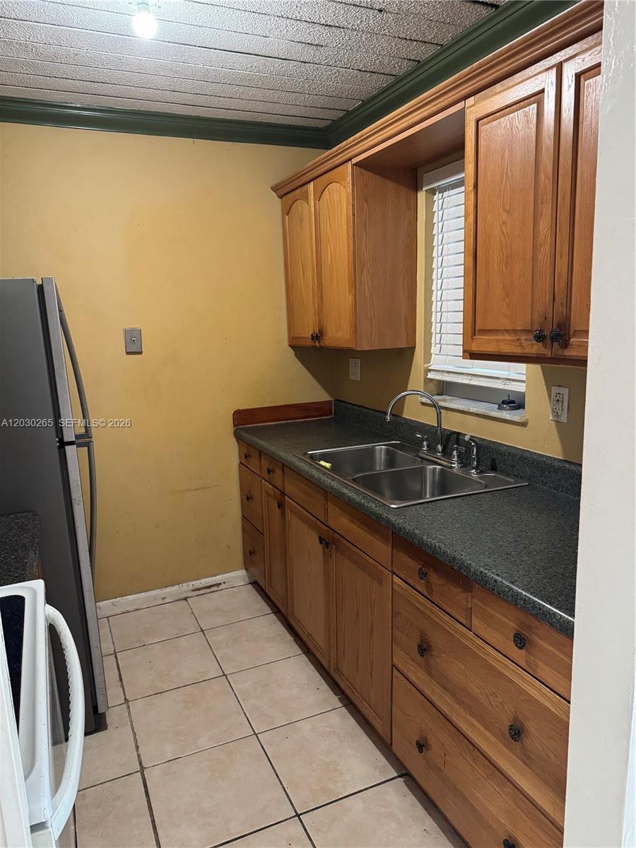 A kitchen features wooden cabinets, a dark countertop, a double sink, and tiled flooring — 7105 W 13th Ave # 403, Hialeah FL 33014, HIALEAH, FL