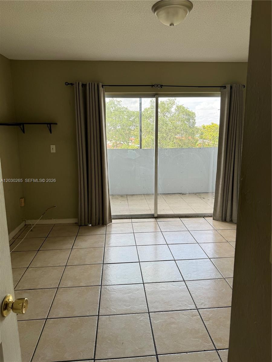 A room with beige tile flooring, light-colored walls, and sliding glass doors leading to a balcony — 7105 W 13th Ave # 403, Hialeah FL 33014, HIALEAH, FL