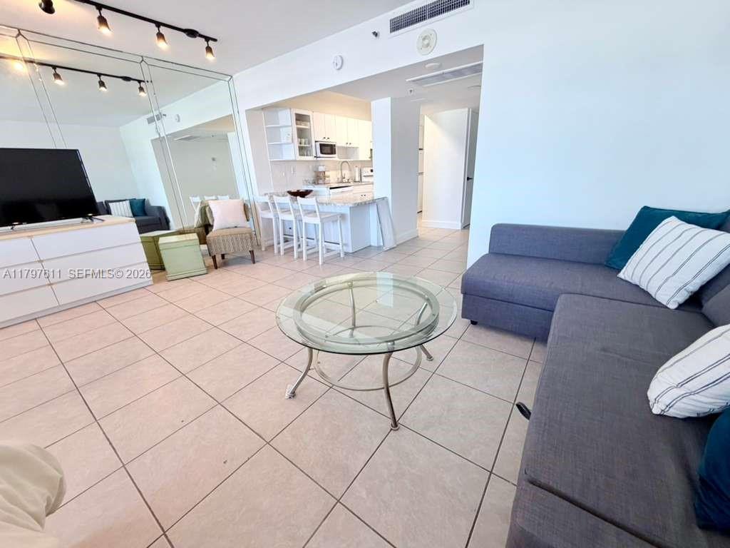 A living room features tile floors, a glass coffee table, and an open kitchen area — 100 Lincoln Rd # 1220, Miami Beach FL 33139, MIAMI BEACH, FL