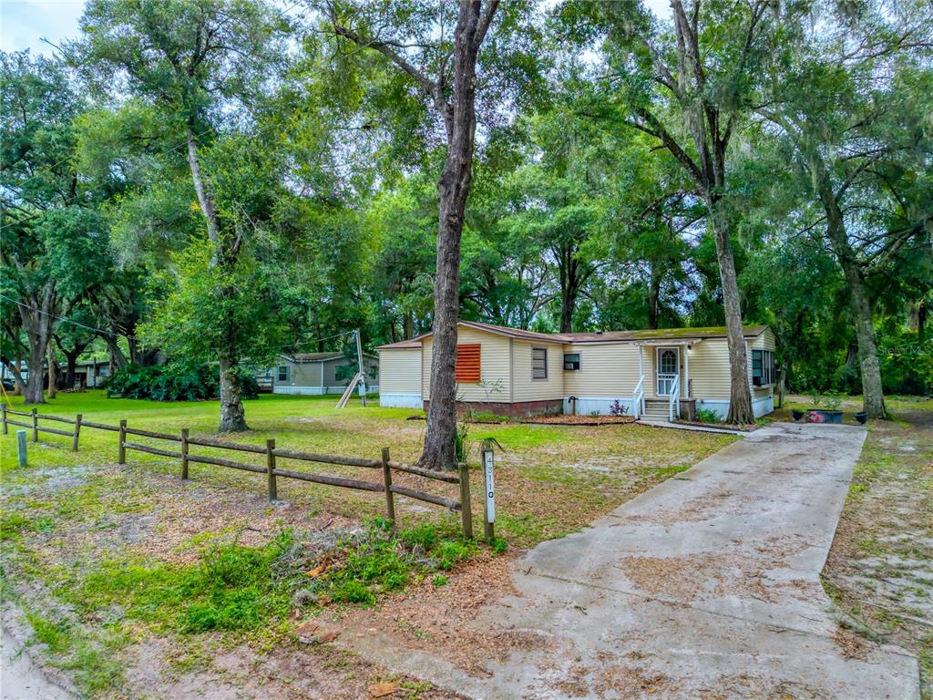 A single-story house with light-colored siding stands behind a wooden fence and concrete driveway — 43110 E 4TH STREET, PAISLEY, FL