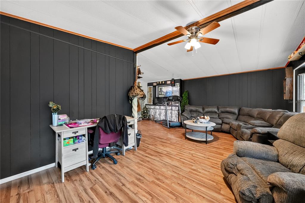 A living room with dark paneled walls, wood-look flooring, a ceiling fan, and a sectional sofa — 43110 E 4TH STREET, PAISLEY, FL
