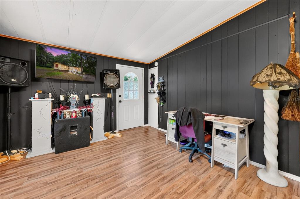 A room with black paneled walls, wood-look flooring, a desk, and a wall-mounted television — 43110 E 4TH STREET, PAISLEY, FL