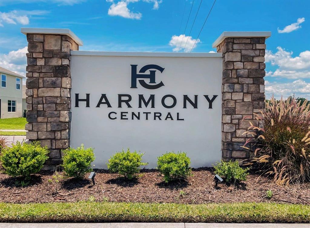 A stone-pillared monument sign displays the Harmony Central logo and text against a blue sky — 3626 BRIARLYNN WAY, ST CLOUD, FL