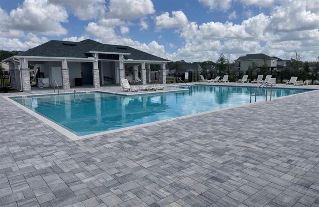 A rectangular swimming pool with a surrounding paver deck and a covered clubhouse pavilion — 3626 BRIARLYNN WAY, ST CLOUD, FL