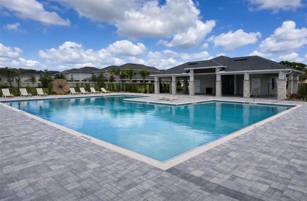 A large outdoor swimming pool with a surrounding stone patio and a covered clubhouse pavilion — 3626 BRIARLYNNE WAY, ST CLOUD, FL