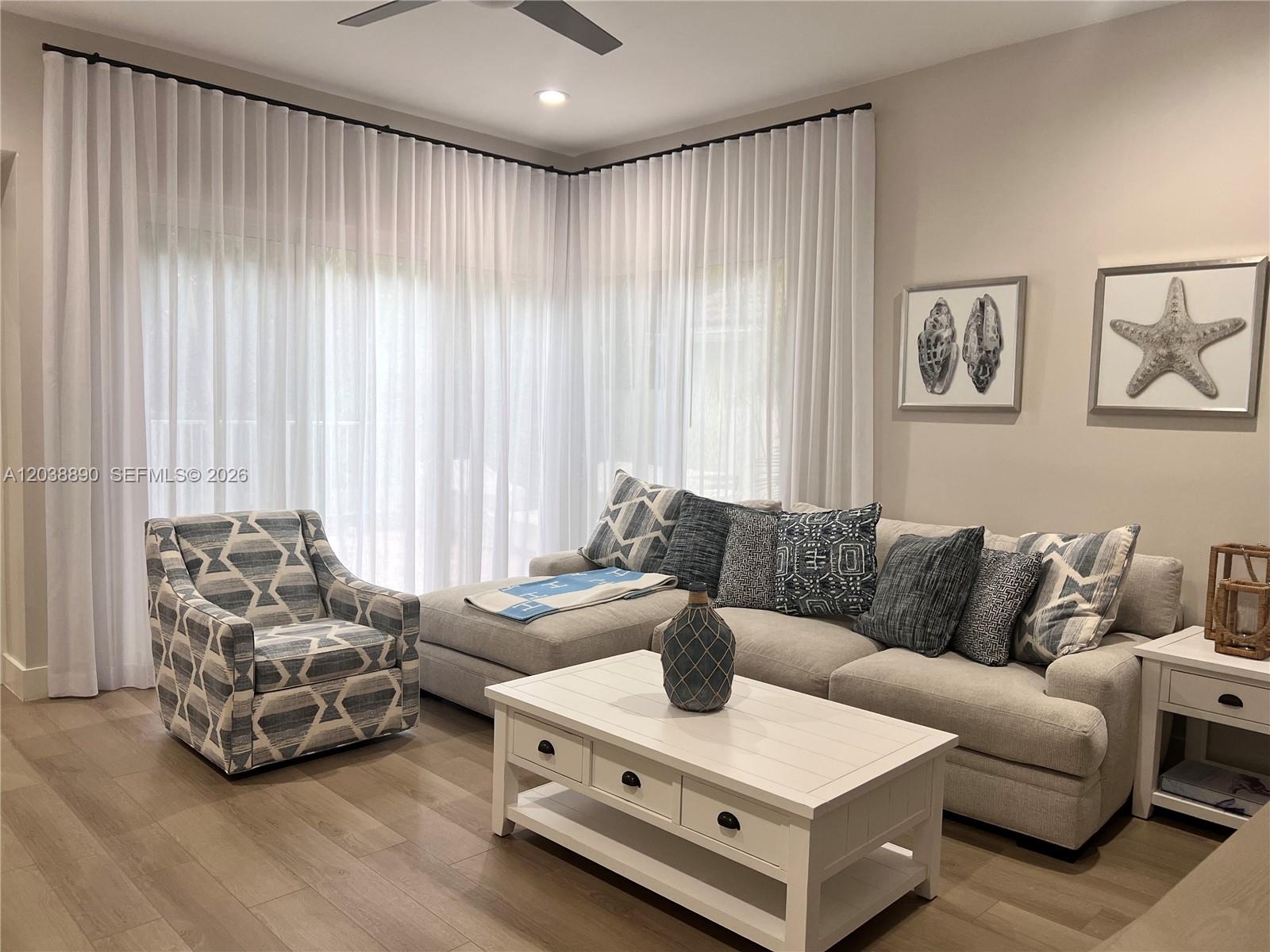 A living room features a sectional sofa, patterned armchair, white coffee table, and floor-to-ceiling curtains — 1480 Sweetbay Way, Hollywood FL 33019, HOLLYWOOD, FL