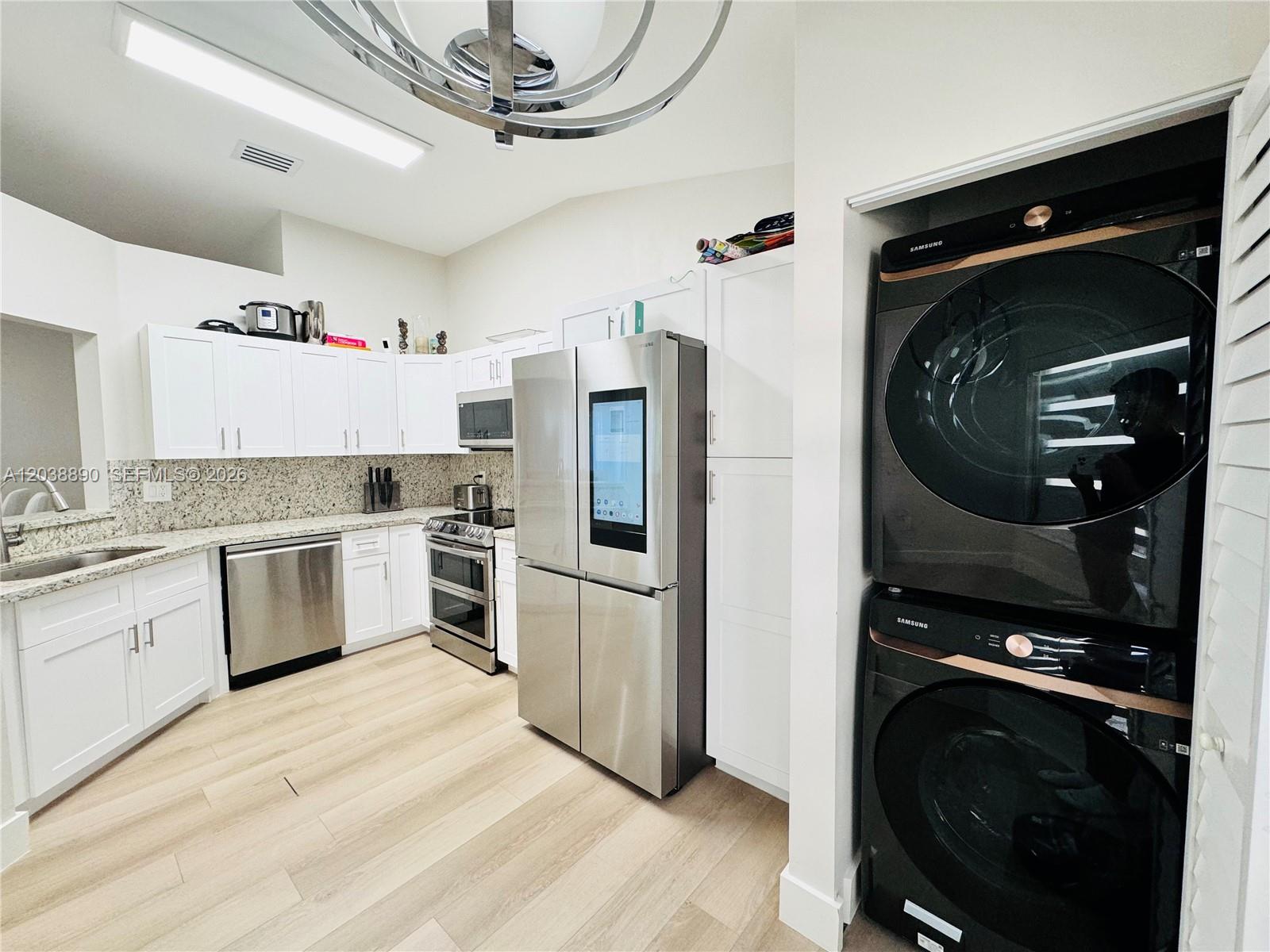 A kitchen features white cabinets, stainless steel appliances, a smart refrigerator, and stacked laundry units — 1480 Sweetbay Way, Hollywood FL 33019, HOLLYWOOD, FL