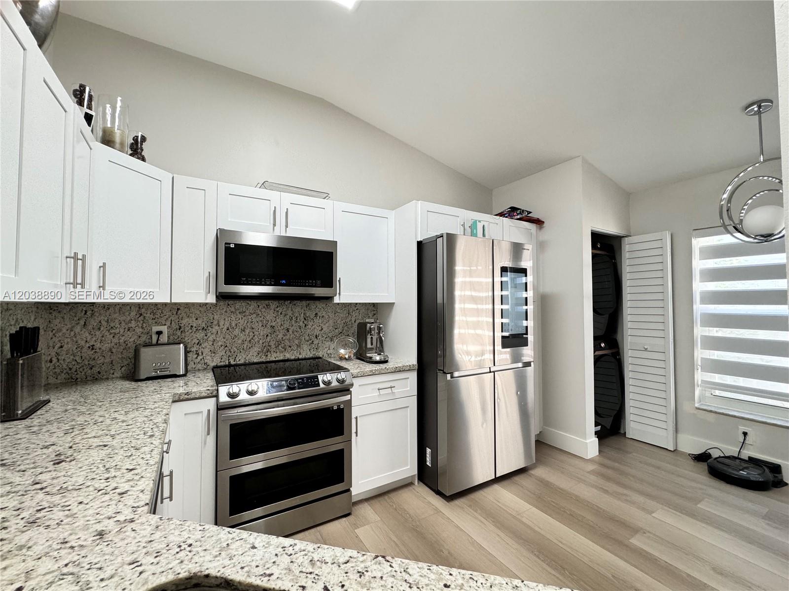 A kitchen features white cabinets, stainless steel appliances, granite countertops, and light wood flooring — 1480 Sweetbay Way, Hollywood FL 33019, HOLLYWOOD, FL