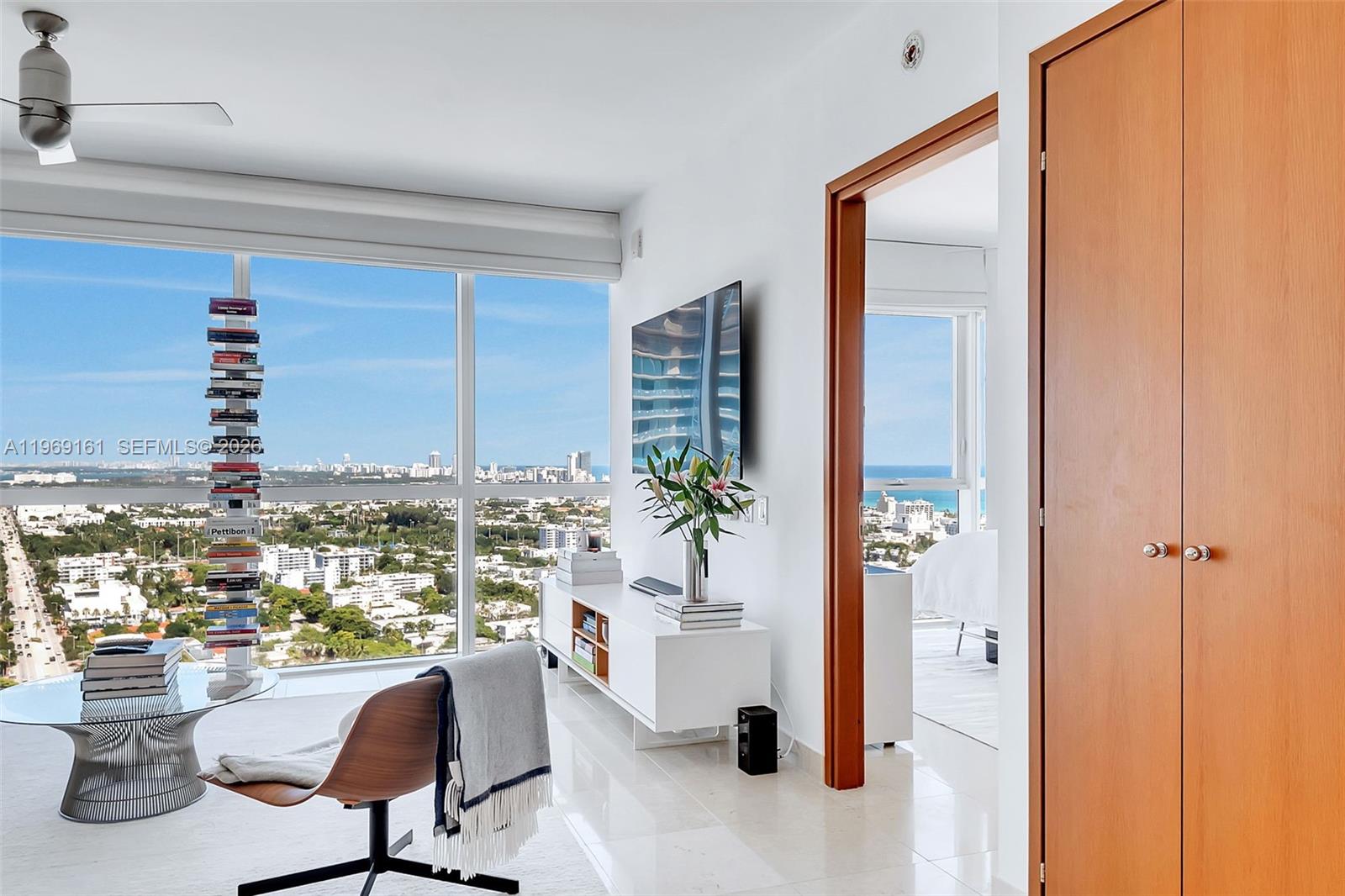 A modern living room features floor-to-ceiling windows with city views and a floating bookshelf — 450 Alton Rd # 3208, Miami Beach FL 33139, MIAMI BEACH, FL