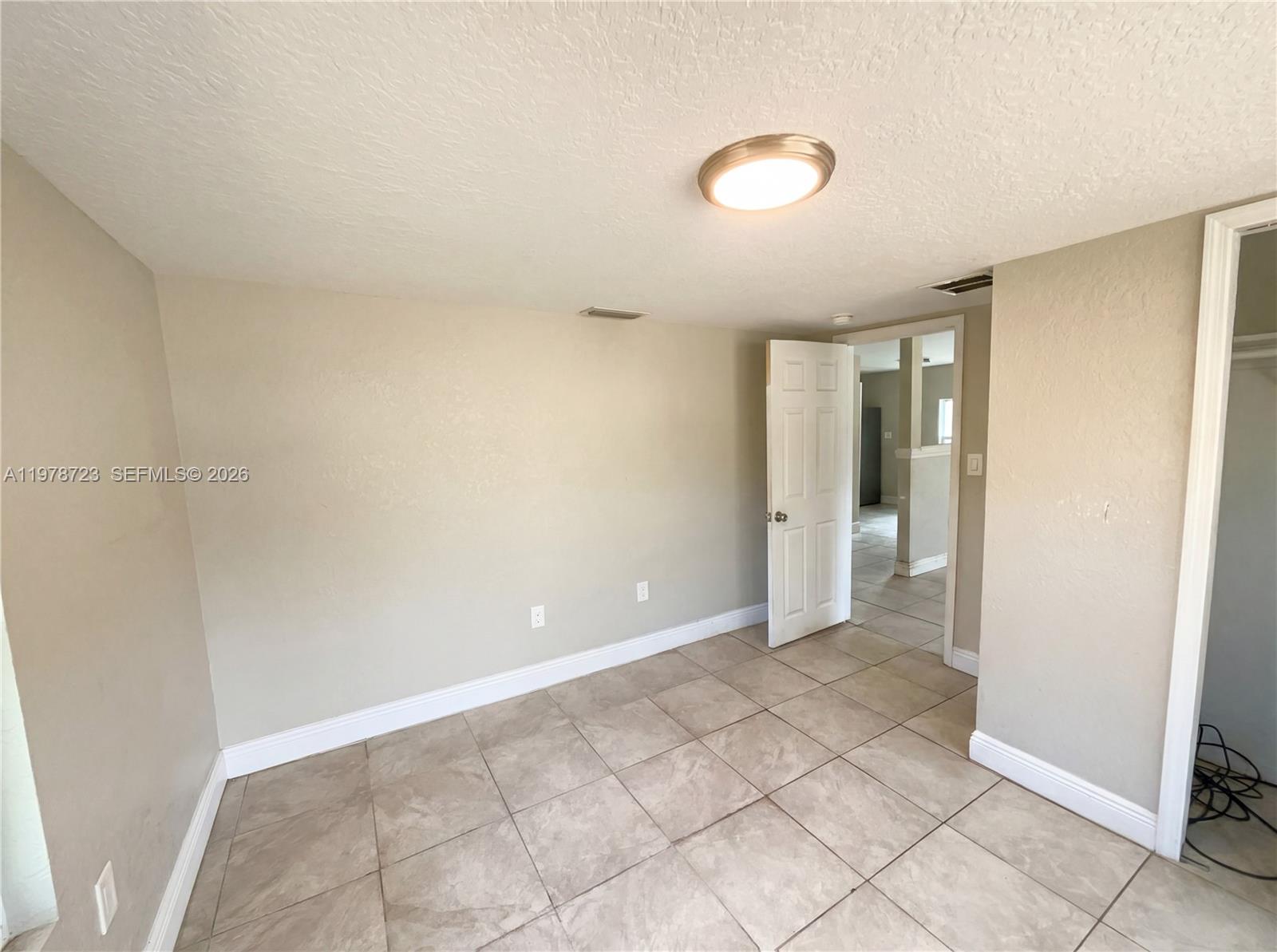 An empty room features beige walls, light-colored tile flooring, a ceiling light, and an open door — 244 S Rhodes, Mount Dora FL 32757, MOUNT DORA, FL