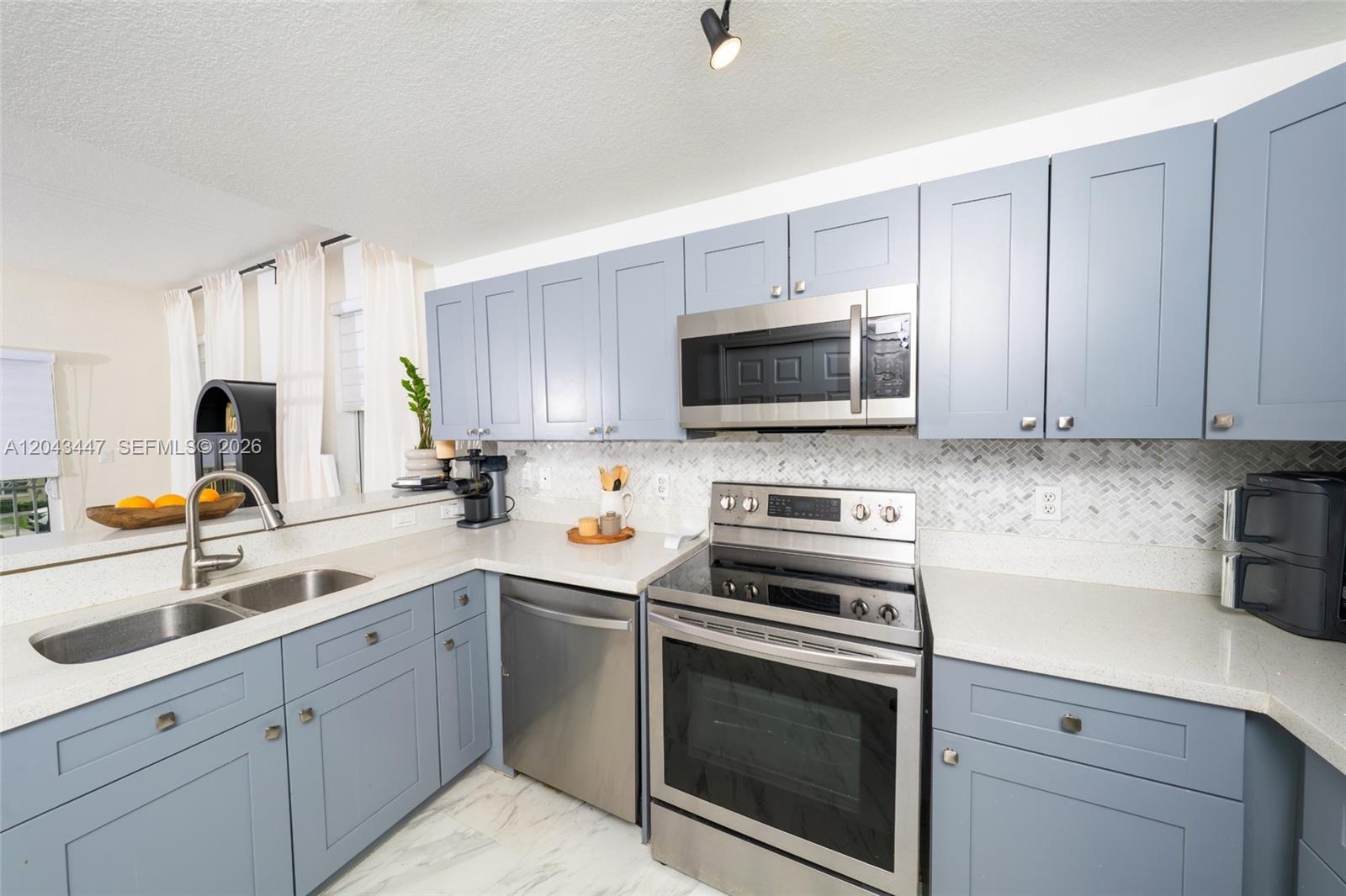 A kitchen features blue cabinets, stainless steel appliances, and a light-colored herringbone tile backsplash — 11101 NW 83rd St # 201, Doral FL 33178, DORAL, FL