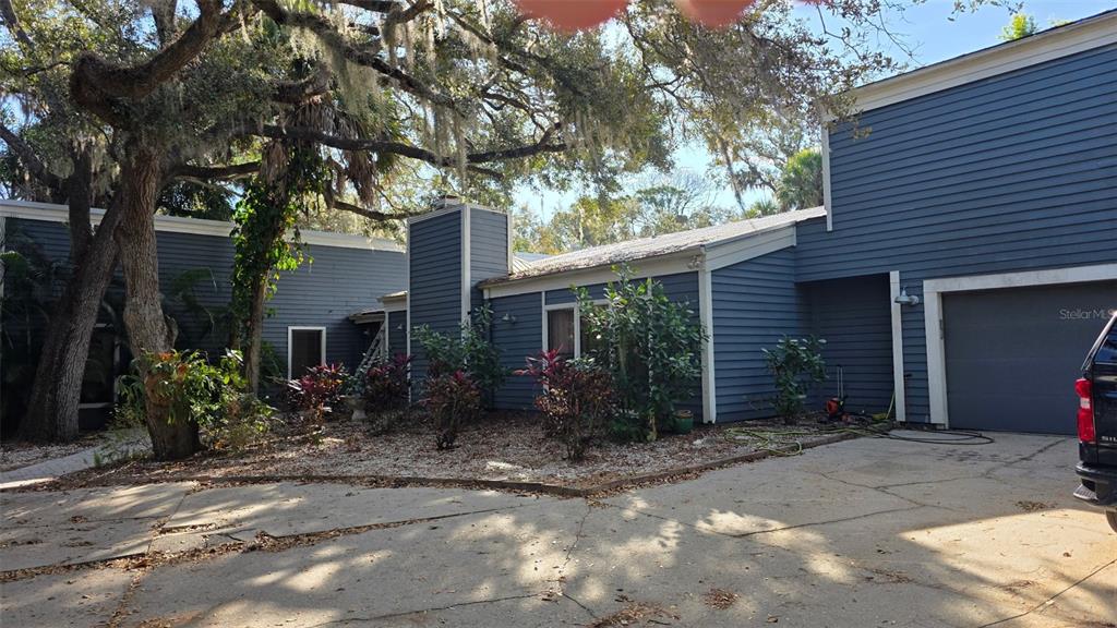 A blue-sided house with a chimney, a concrete driveway, and large oak trees in front — 4889 BRIGITTA DRIVE, SARASOTA, FL