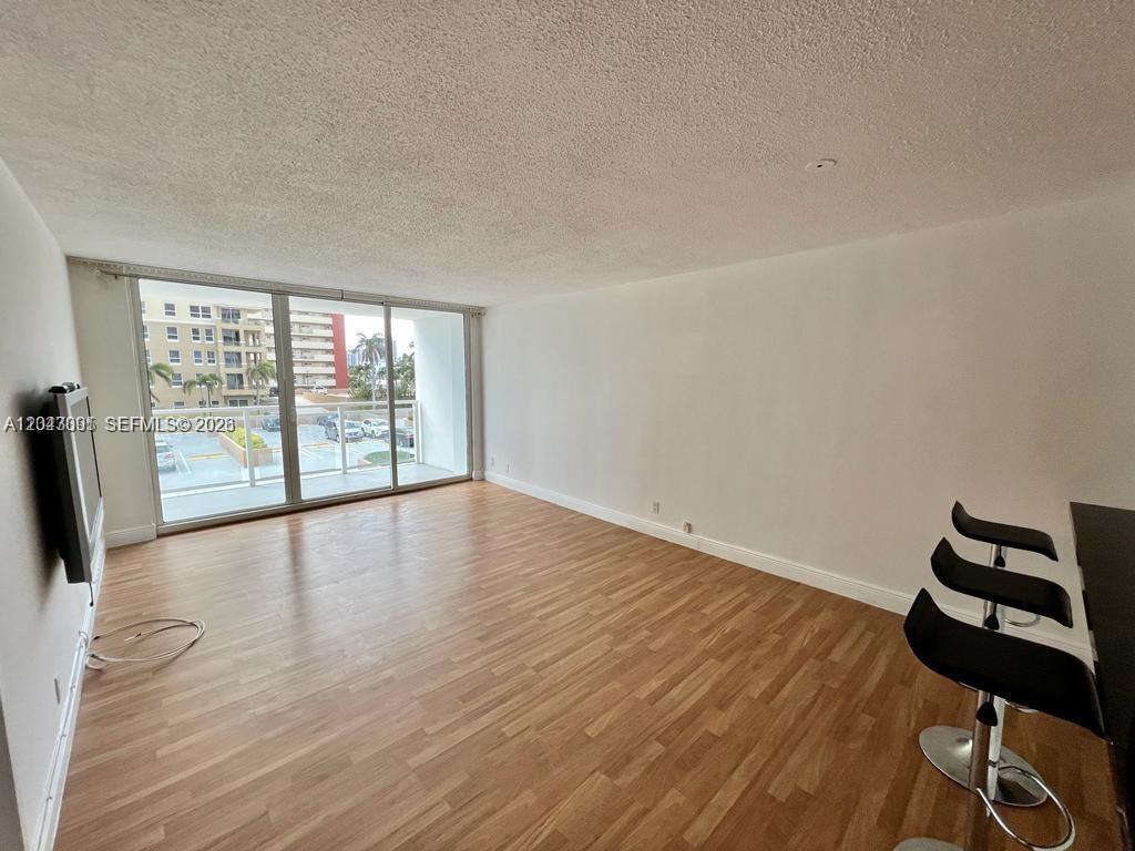 An empty living room features light wood-look flooring, white walls, and a sliding glass balcony door — 2030 S Ocean Dr # 211, Hallandale Beach FL 33009, HALLANDALE BEACH, FL