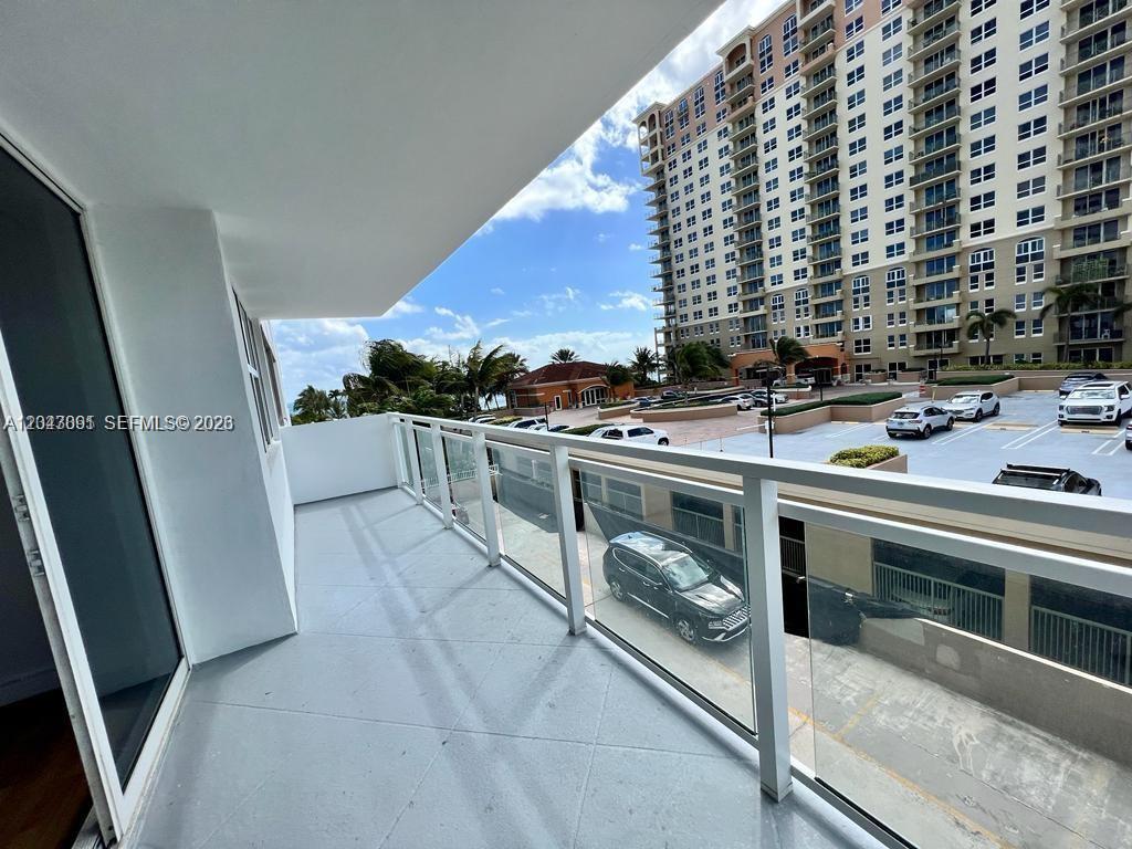 A balcony with a glass railing overlooks a parking lot and a tall apartment building — 2030 S Ocean Dr # 211, Hallandale Beach FL 33009, HALLANDALE BEACH, FL