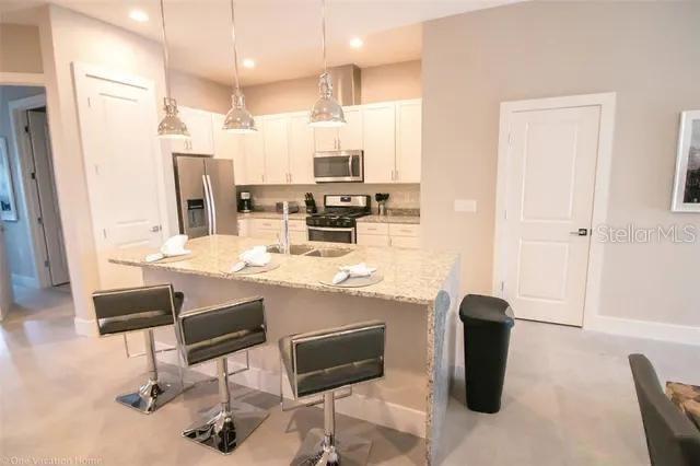 A kitchen features white cabinets, granite countertops, a center island with bar stools, and appliances — 7520 SUNVILLE AVENUE, KISSIMMEE, FL