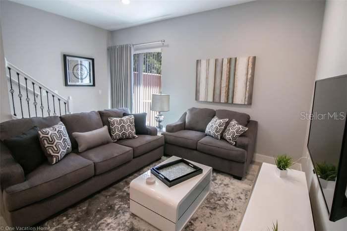 A living room features two gray sofas, a white coffee table, and a wall-mounted television — 7520 SUNVILLE AVENUE, KISSIMMEE, FL