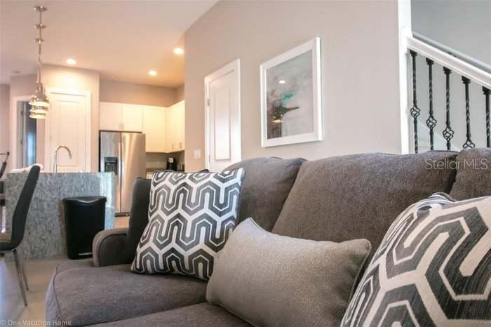 A gray sofa with patterned pillows sits in a living room facing an open kitchen — 7520 SUNVILLE AVENUE, KISSIMMEE, FL