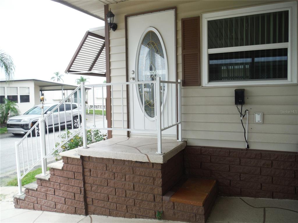 A white front door with an oval glass insert sits above brick steps and railings — 161 HICKORY GATE DRIVE, PALM HARBOR, FL