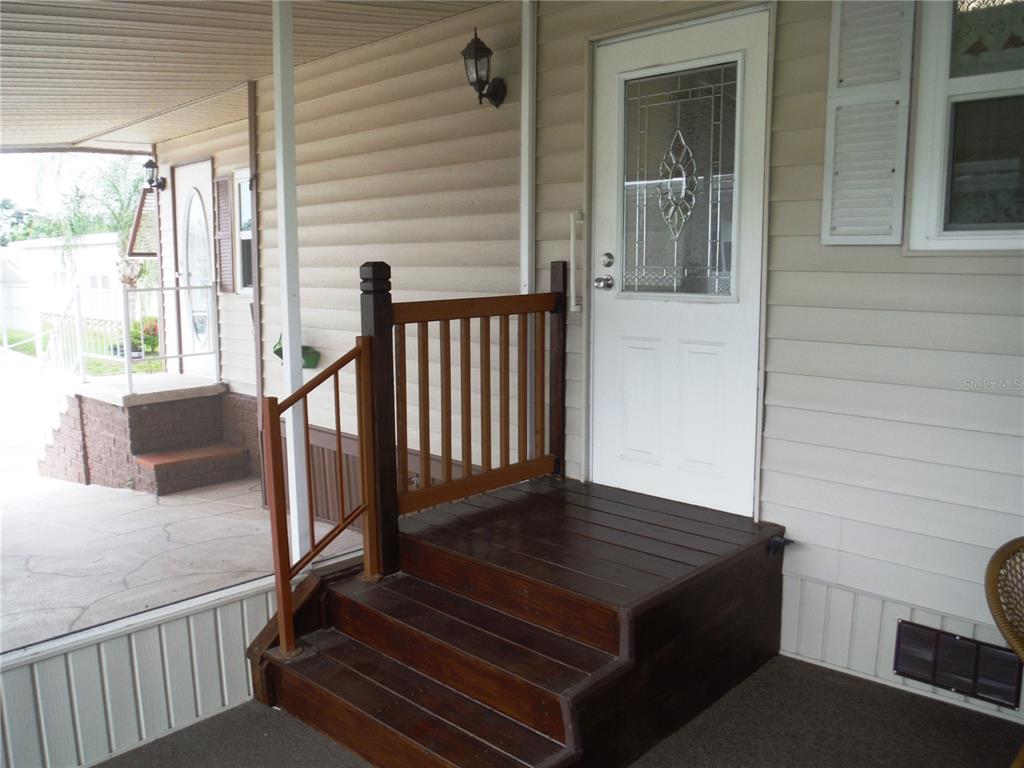 A wooden staircase with a railing leads to a white door on a covered porch — 161 HICKORY GATE DRIVE, PALM HARBOR, FL