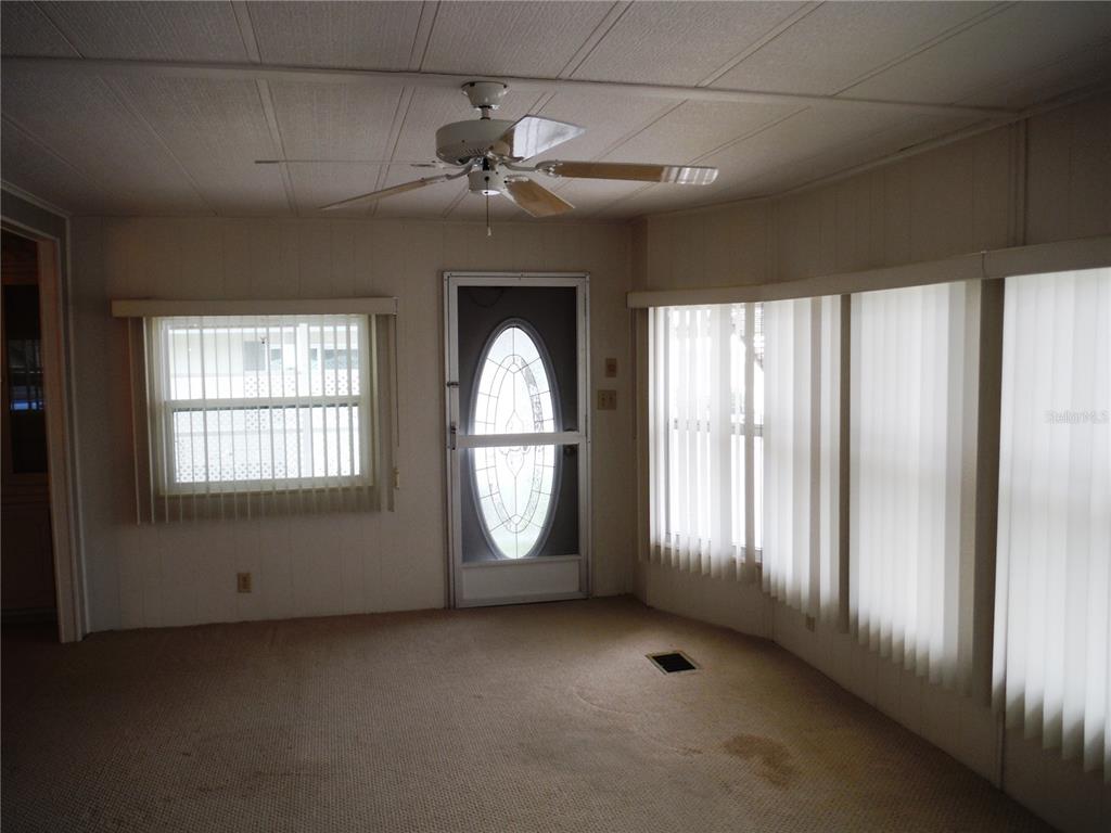 A living room with beige carpet, a ceiling fan, a glass-paneled door, and vertical blinds — 161 HICKORY GATE DRIVE, PALM HARBOR, FL