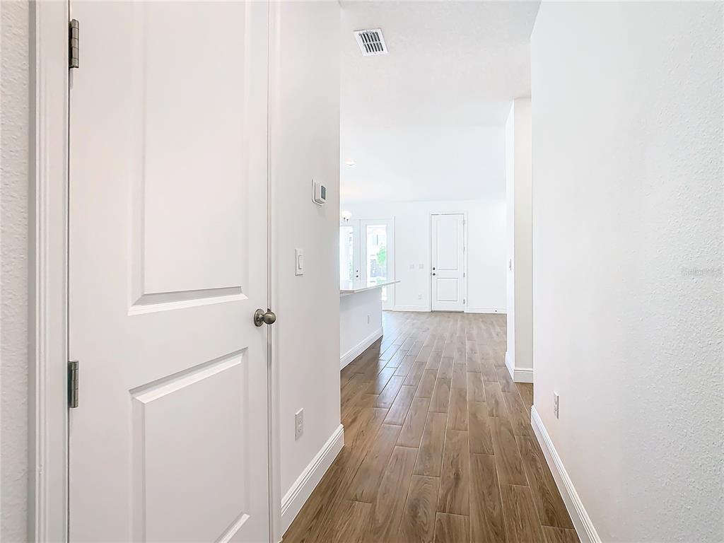 A hallway with wood-look tile flooring leads toward an open-concept kitchen and living area — 11165 GREEN CITRON ALLEY, WINTER GARDEN, FL