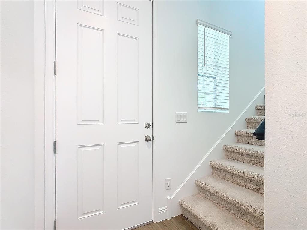 A white front door stands next to a carpeted staircase in a bright entryway — 11165 GREEN CITRON ALLEY, WINTER GARDEN, FL