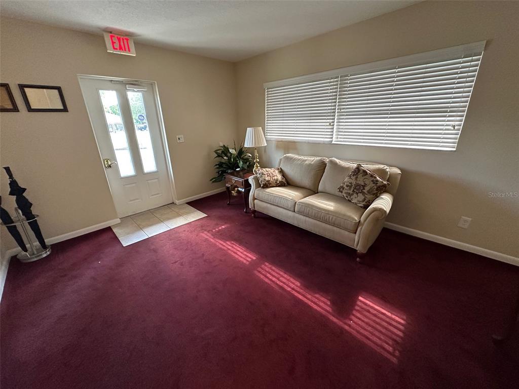 A room with maroon carpeting, a beige sofa, and an exterior door with an exit sign — 502 E AIRPORT BOULEVARD, SANFORD, FL