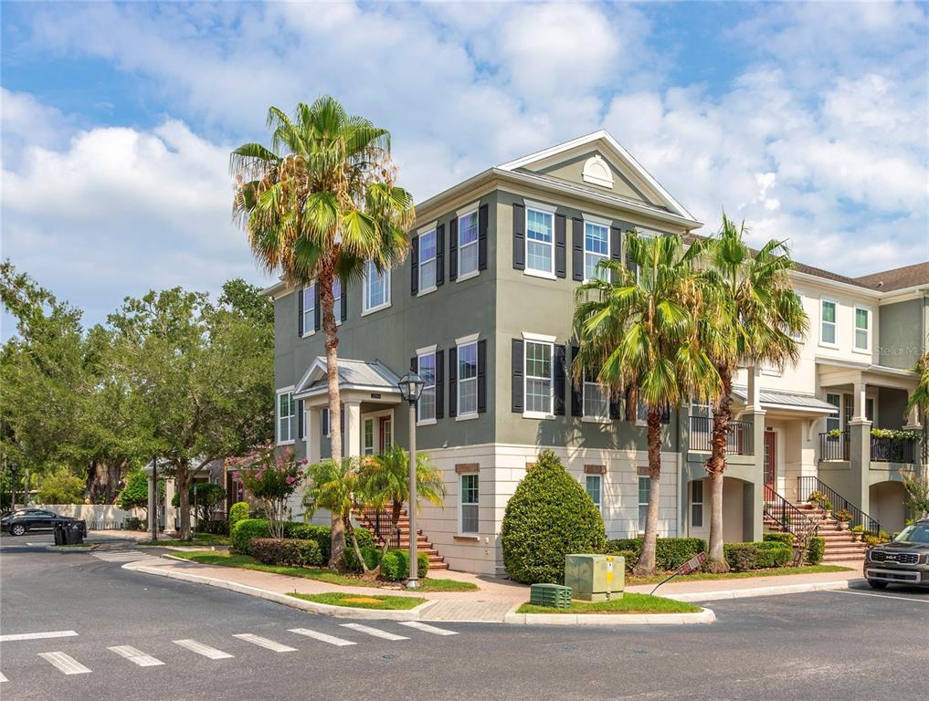 A three-story townhouse with green stucco siding, black shutters, and palm trees in the front — 2595 JOSLIN PLACE, ORLANDO, FL