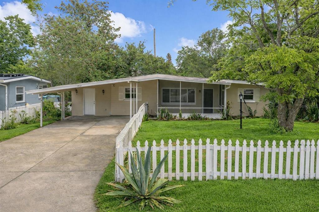 A single-story house with a carport, white picket fence, and a screened-in front porch — 1712 TALLAHASSEE DRIVE, DAYTONA BEACH, FL