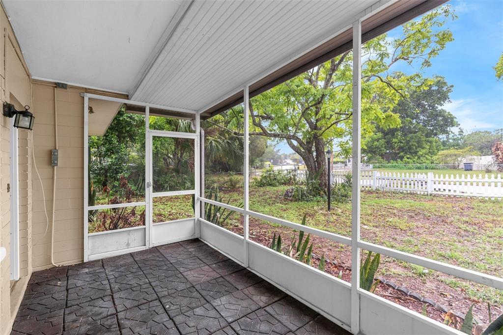 A screened-in porch with a patterned tile floor overlooks a grassy backyard with trees — 1712 TALLAHASSEE DRIVE, DAYTONA BEACH, FL
