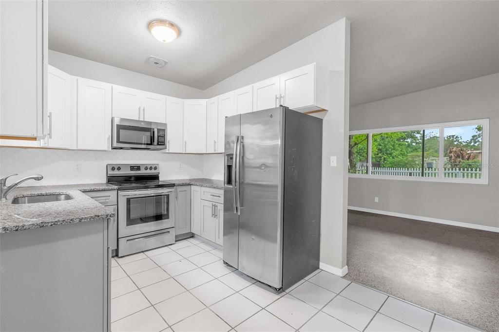 A kitchen with white cabinets, granite countertops, stainless steel appliances, and tile flooring — 1712 TALLAHASSEE DRIVE, DAYTONA BEACH, FL