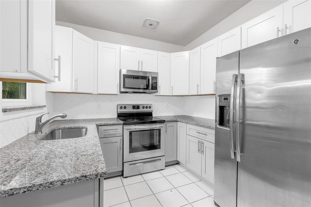 A kitchen with white cabinets, granite countertops, stainless steel appliances, and white tiled flooring — 1712 TALLAHASSEE DRIVE, DAYTONA BEACH, FL
