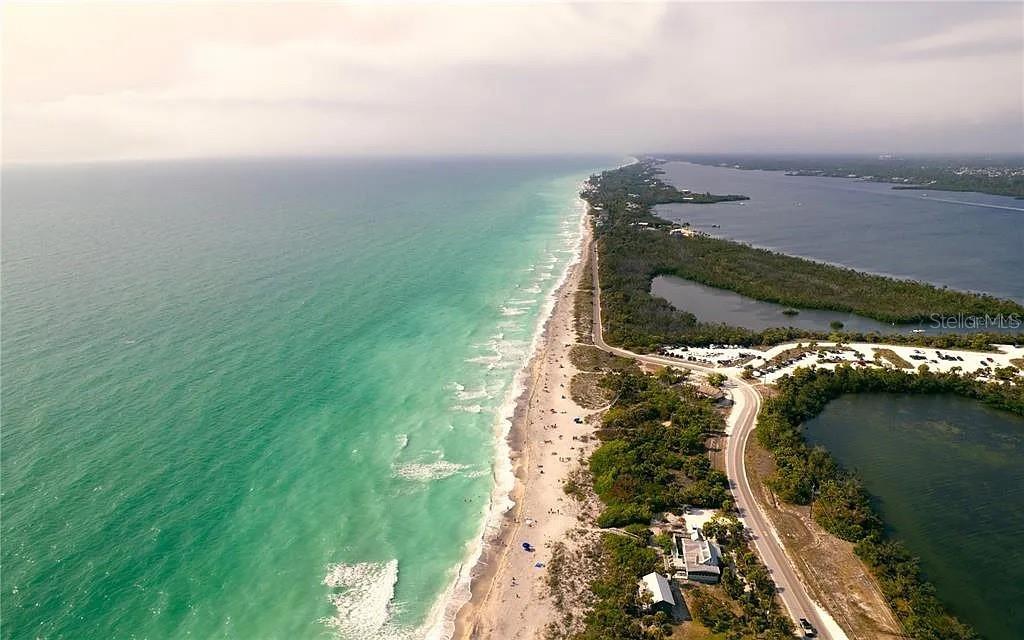 An aerial view shows a narrow barrier island with a beach, road, and coastal vegetation — MC GINNIS TERRACE, NORTH PORT, FL