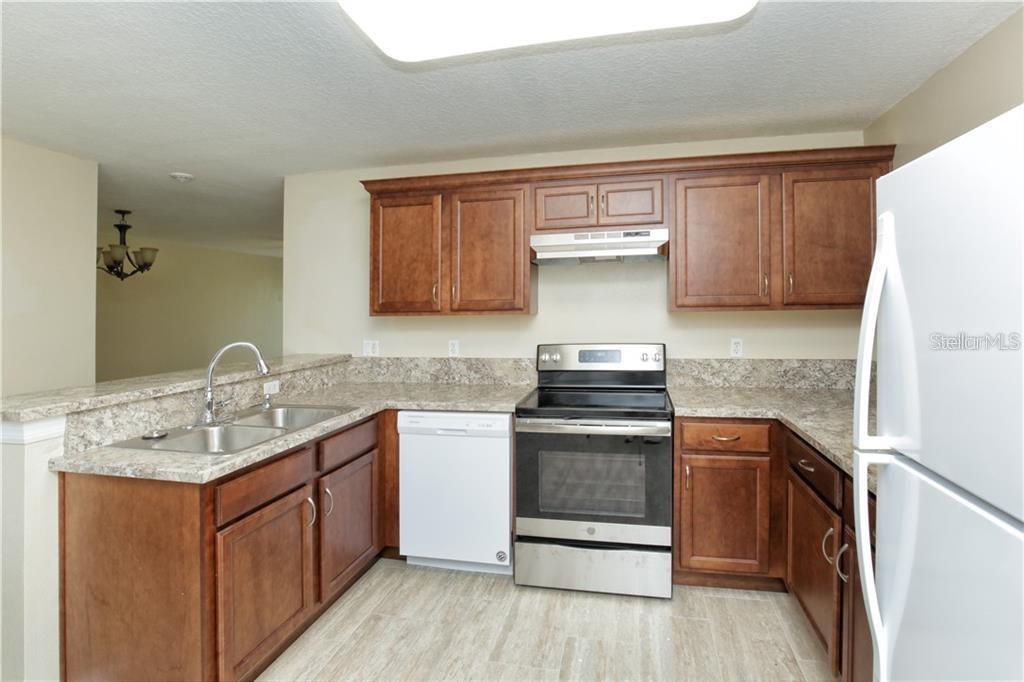 A kitchen features wood cabinets, granite countertops, stainless steel appliances, and light-colored tile flooring — 8829 GRAND PALMS CIRCLE UNIT A, KISSIMMEE, FL