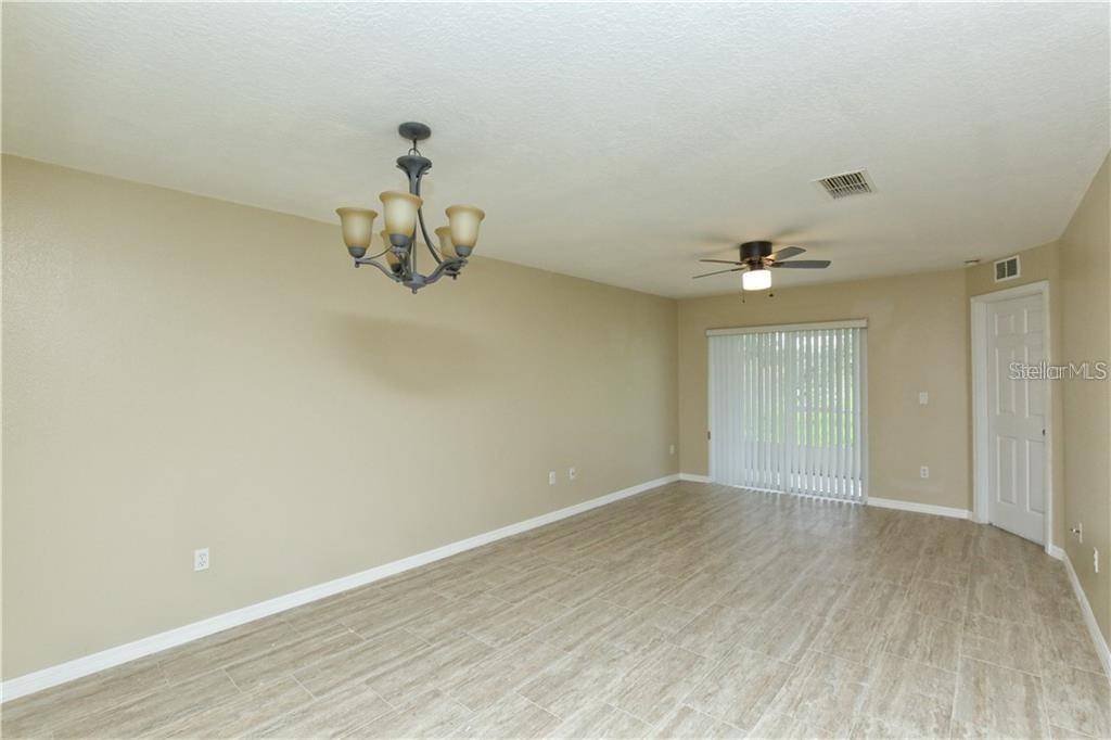 A living room features light-colored tile flooring, beige walls, a ceiling fan, and a chandelier — 8829 GRAND PALMS CIRCLE UNIT A, KISSIMMEE, FL