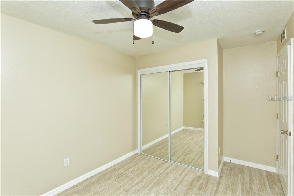 A bedroom features light-colored walls, wood-look flooring, a ceiling fan, and mirrored closet doors — 8829 GRAND PALMS CIRCLE UNIT A, KISSIMMEE, FL