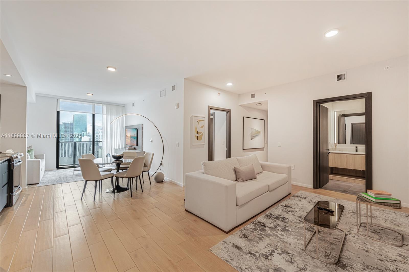 A modern living room features light wood flooring, a white sofa, and a dining area — 398 NE 5th St # 3017, Miami FL 33132, MIAMI, FL