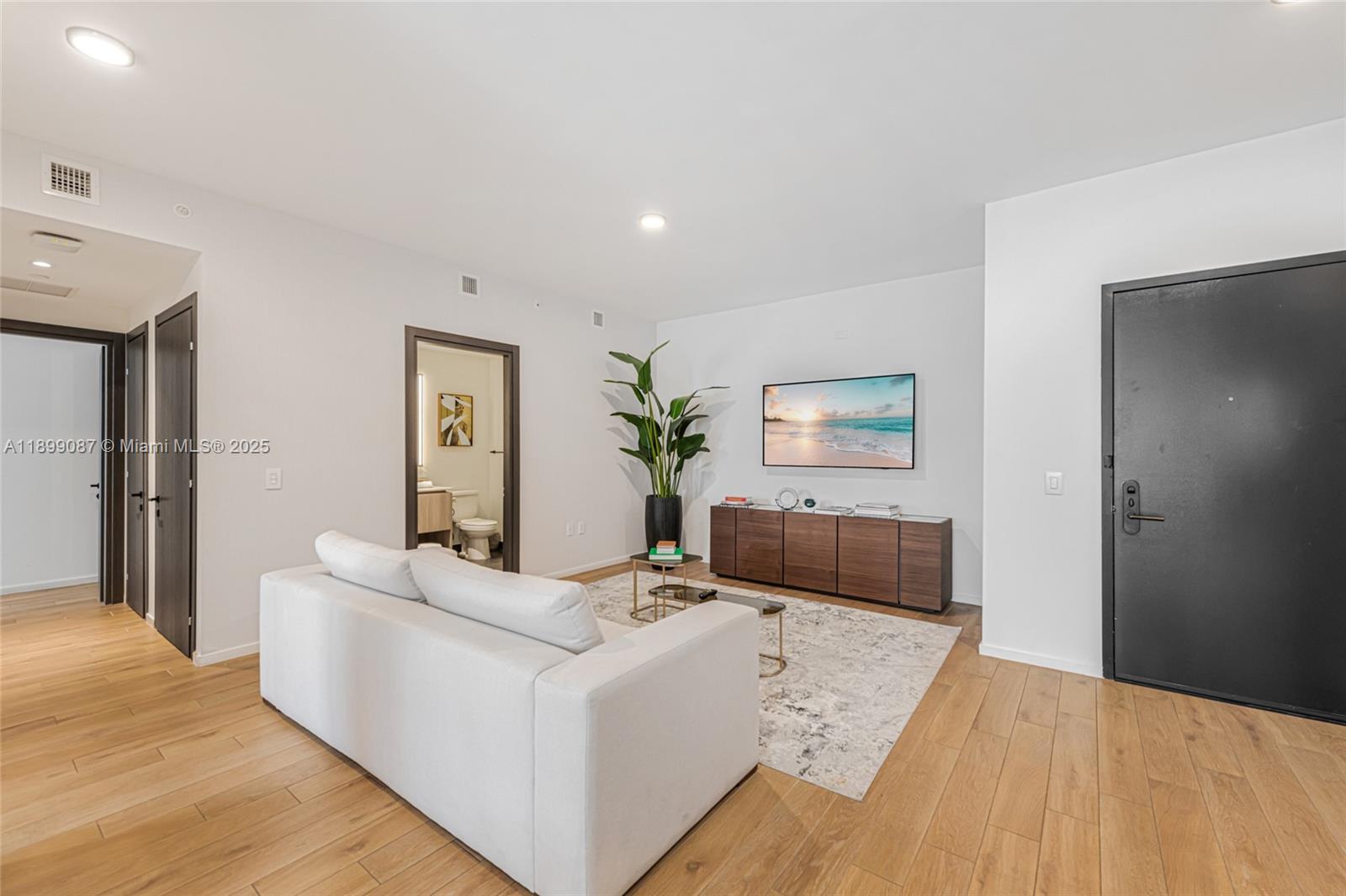 A modern living room features a white sofa, wood flooring, and a wall-mounted television — 398 NE 5th St # 3017, Miami FL 33132, MIAMI, FL