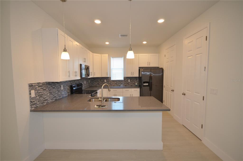 A kitchen features white cabinets, gray countertops, a tiled backsplash, and stainless steel appliances — 8581 AGATE STREET, PORT CHARLOTTE, FL