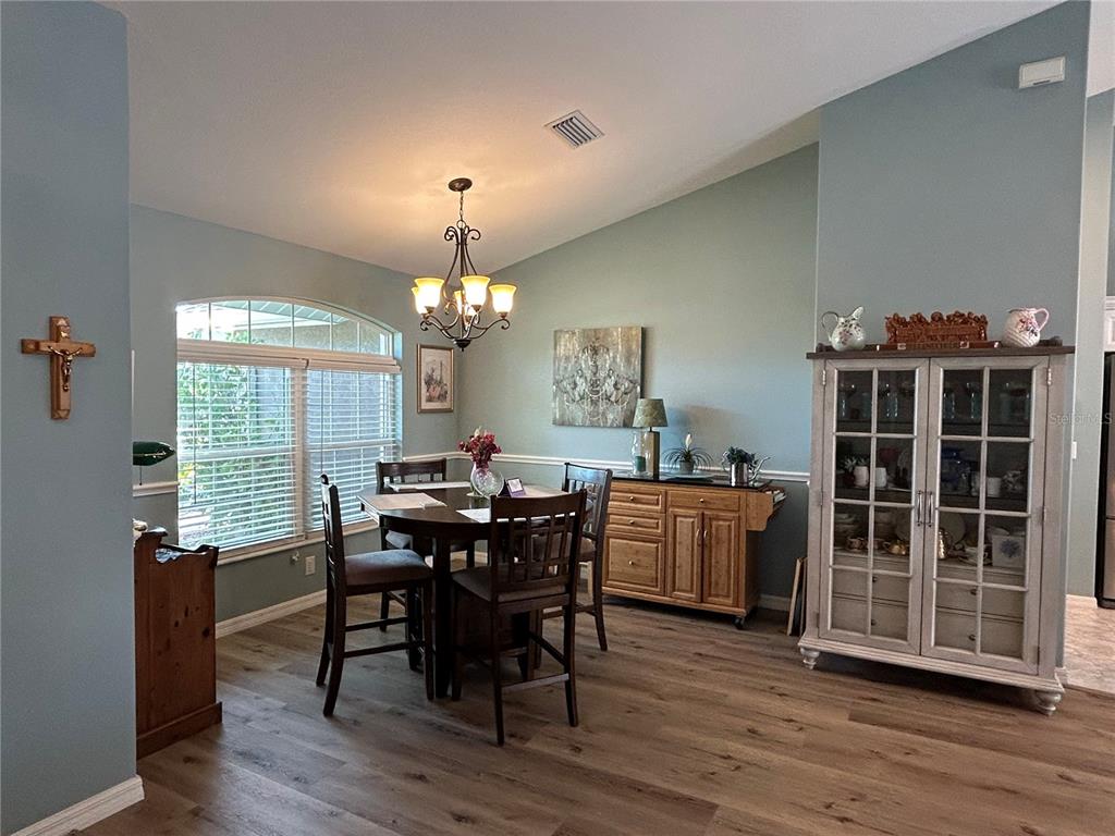 A dining room features light blue walls, wood-look flooring, a round table, and a china cabinet — 108 BERYL DRIVE, ROTONDA WEST, FL