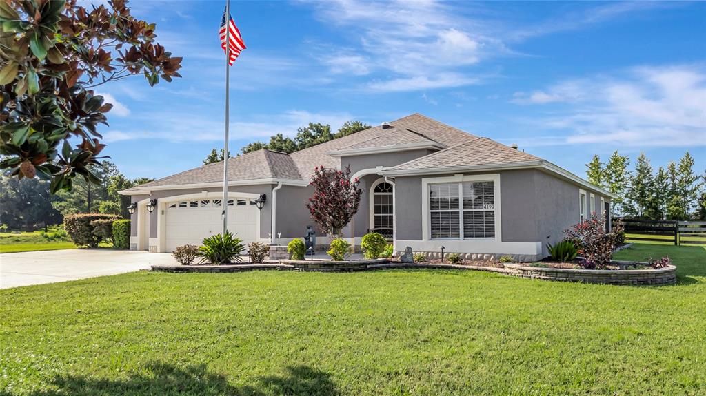 A single-story gray house with a two-car garage, a flag pole, and landscaped front yard — 4190 COUNTY ROAD 121D, WILDWOOD, FL