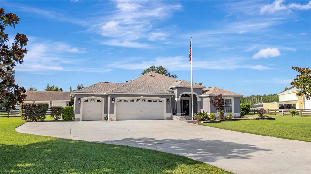 A single-story gray house with a three-car garage and a large concrete driveway — 4190 COUNTY ROAD 121D, WILDWOOD, FL