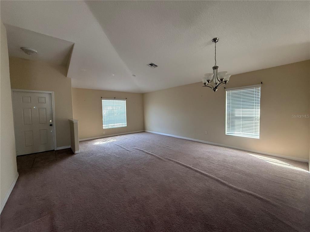 An empty room with beige carpet, light-colored walls, two windows with blinds, and a chandelier — 2370 DOVESONG TRACE DRIVE, RUSKIN, FL