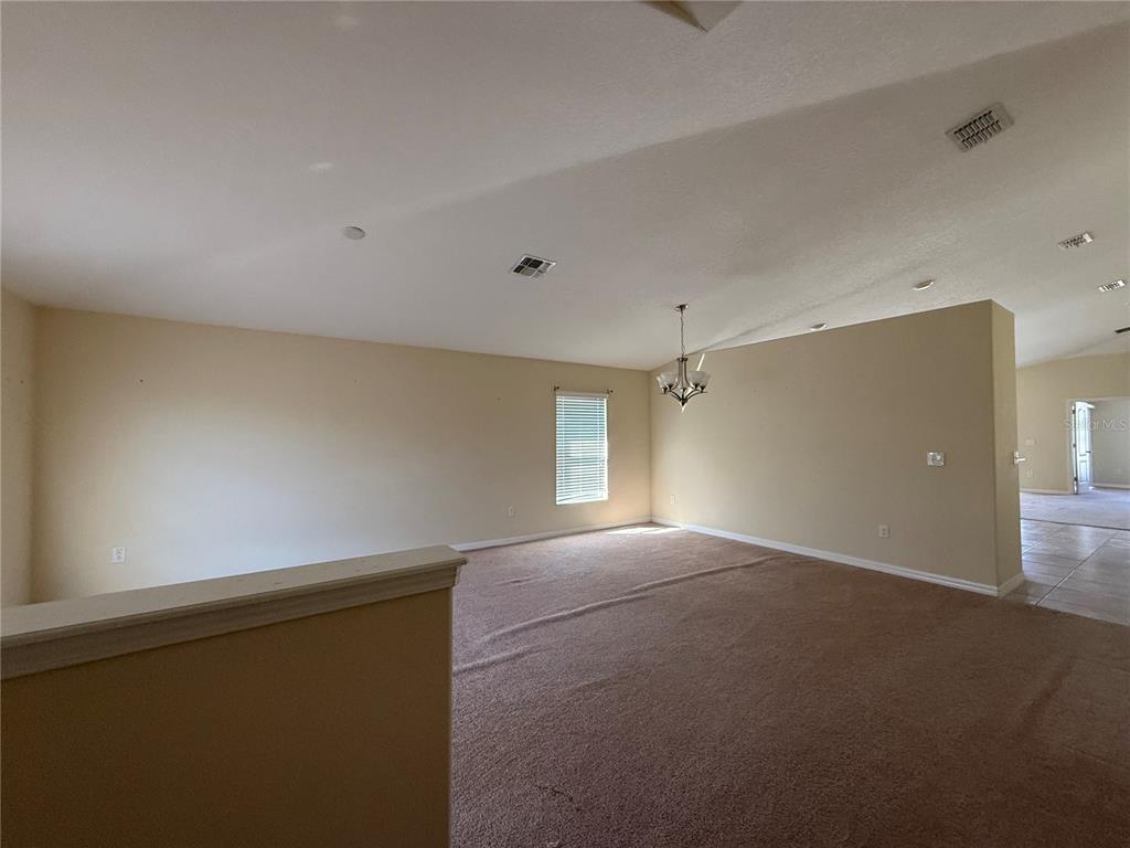 A spacious, carpeted living area features a vaulted ceiling, a chandelier, and a single window — 2370 DOVESONG TRACE DRIVE, RUSKIN, FL