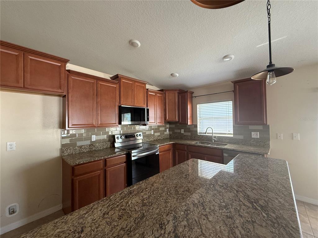 A kitchen features wood cabinets, granite countertops, a tile backsplash, and a breakfast bar — 2370 DOVESONG TRACE DRIVE, RUSKIN, FL