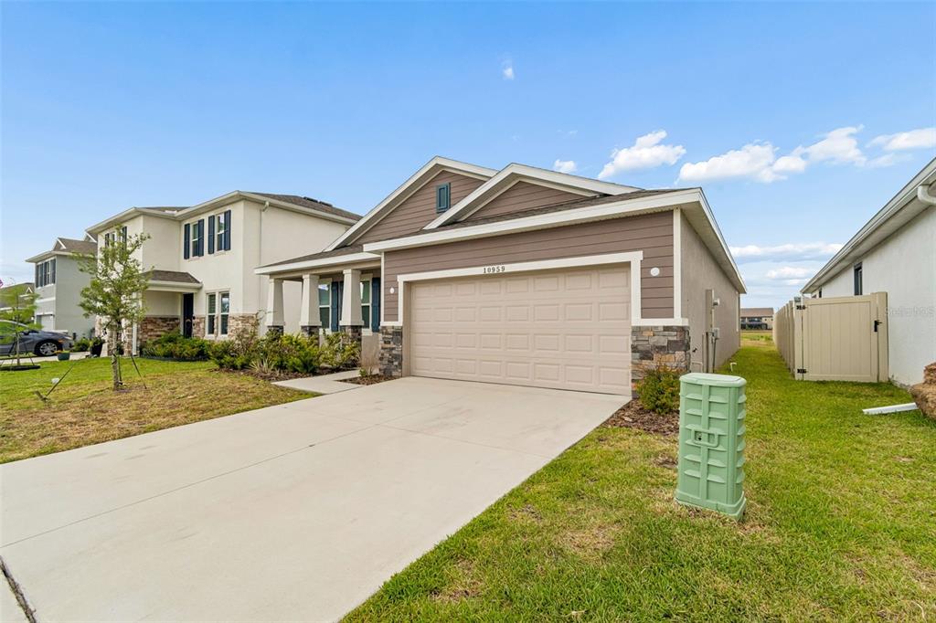 A single-story house with a tan garage, stone accents, and a green utility box outside — 10959 COTTON VALE PLACE, SAN ANTONIO, FL