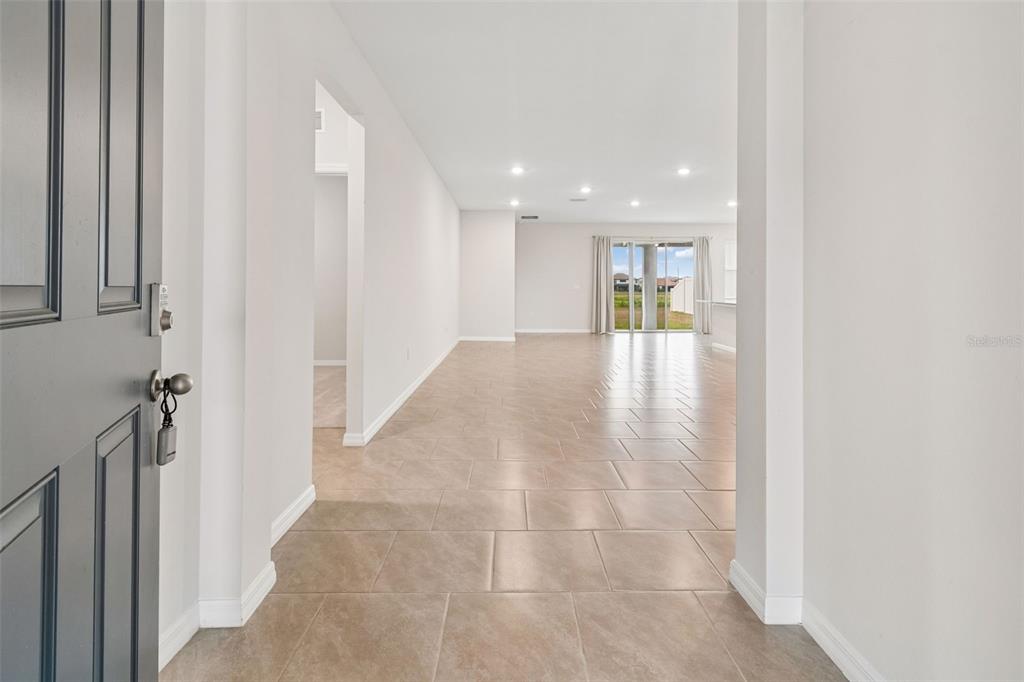 A view from an entryway into an open-concept living area with light-colored tile flooring — 10959 COTTON VALE PLACE, SAN ANTONIO, FL
