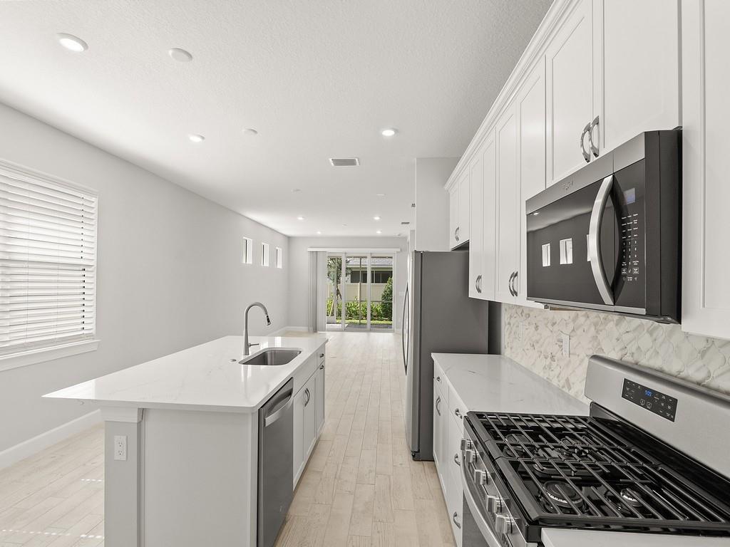 A modern kitchen features white cabinetry, a marble-topped island with a sink, and stainless appliances — 4501 Nautilus Circle, Vero Beach FL 32967, VERO BEACH, FL