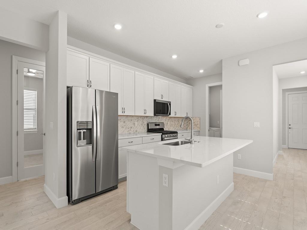 A modern kitchen features white cabinets, stainless steel appliances, a quartz island, and light flooring — 4501 Nautilus Circle, Vero Beach FL 32967, VERO BEACH, FL