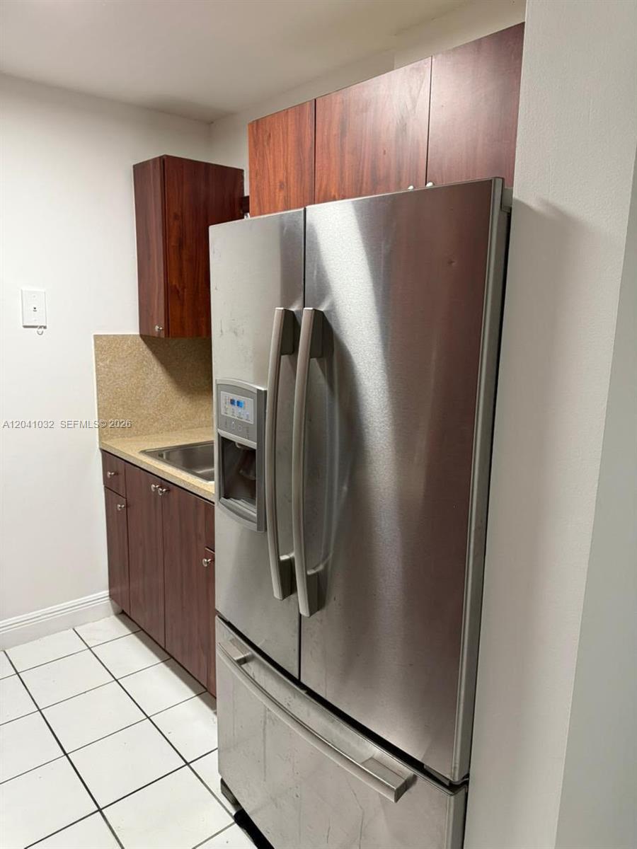 A kitchen features dark wood cabinets, a stainless steel refrigerator, and white tile flooring — 600 NW 32nd Pl # 303, Miami FL 33125, MIAMI, FL